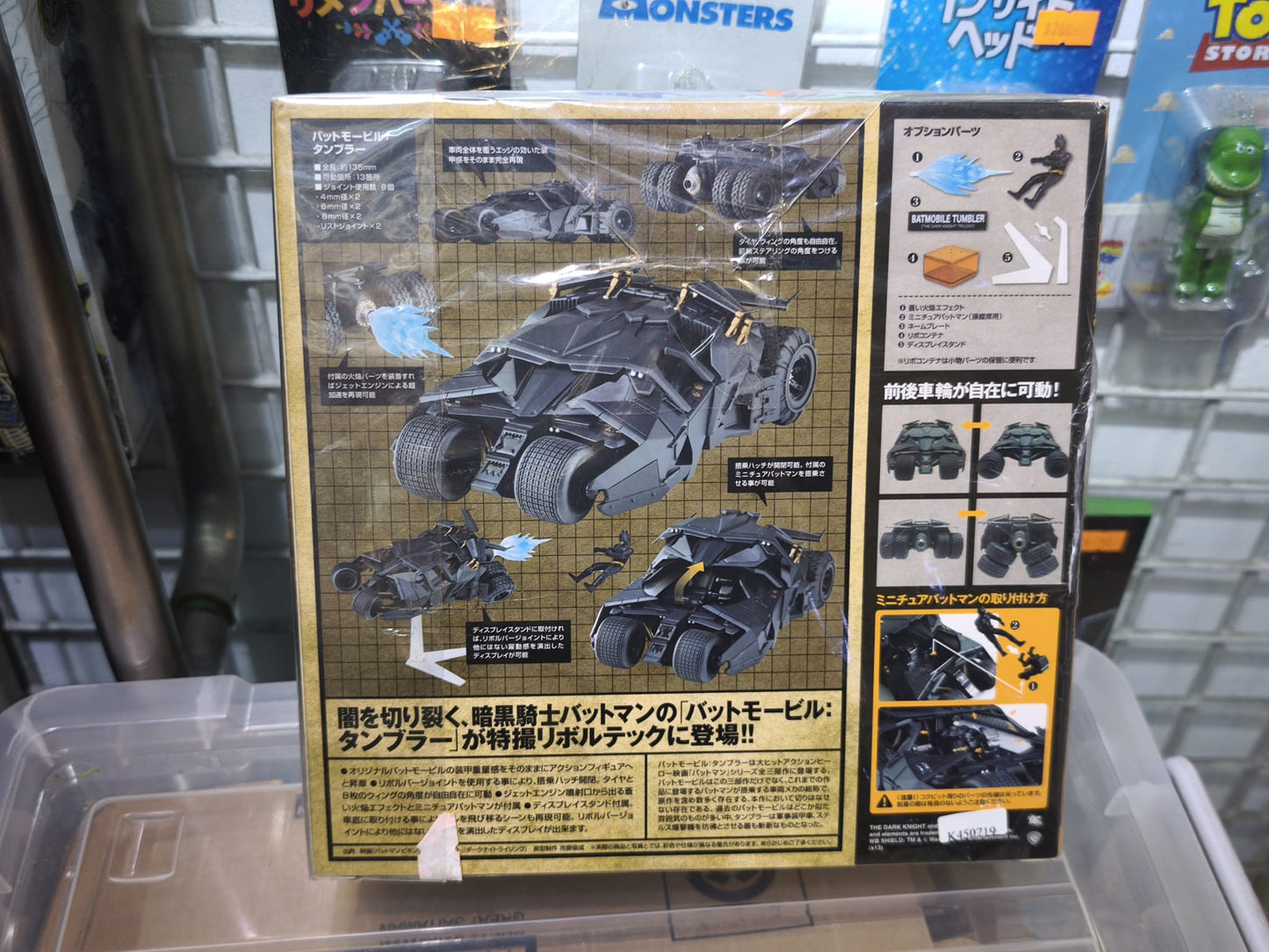 Front retail packaging window box of the Kaiyodo Sci-Fi Revoltech Series No. 043EX Batmobile Tumbler Camouflage Version action figure, displaying the desert-camo armored vehicle, included mini Batman figure, and blue flame effect part.