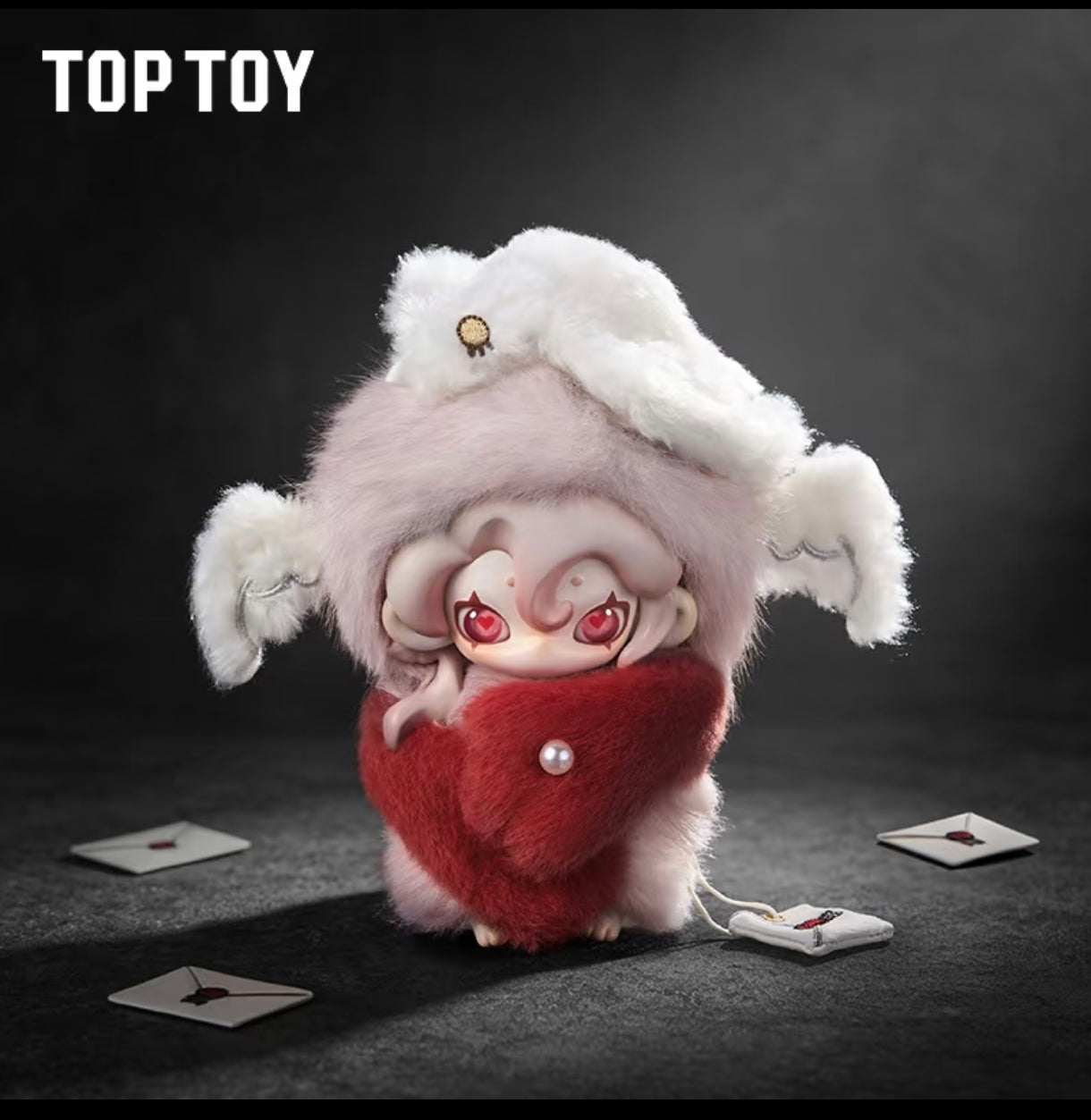 Moonin plush doll with red heart-shaped eyes wrapped in a plush red fur cape with a pearl button accent, surrounded by miniature letters.