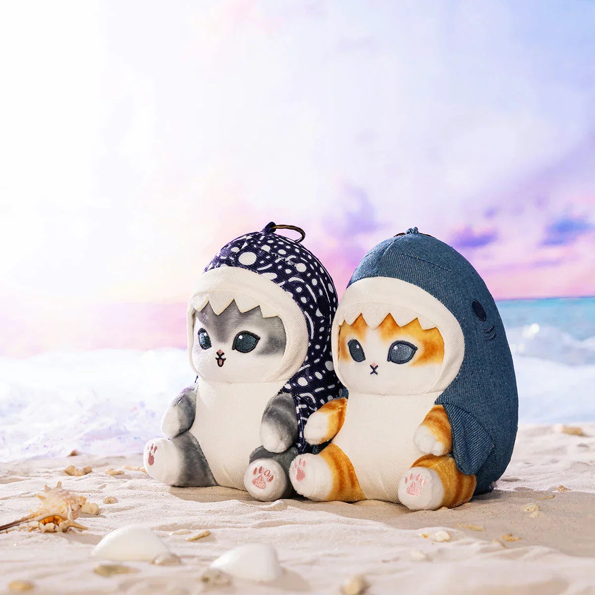 Two Mofusand Sea Animals Series cat plush keychains in shark costumes sitting on a beach, blue denim and patterned designs