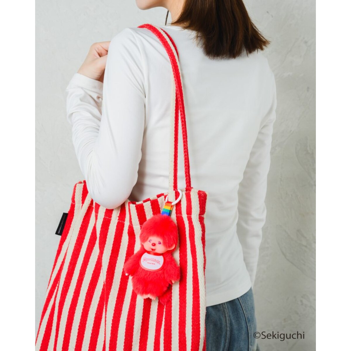 Red macaron Monchhichi Colorful Fantasy plush keychain clipped to a red striped tote bag