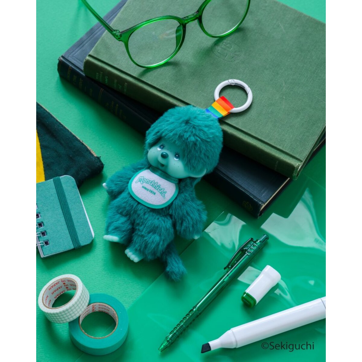 Green macaron Monchhichi Colorful Fantasy plush keychain hanging on a notebook and glasses