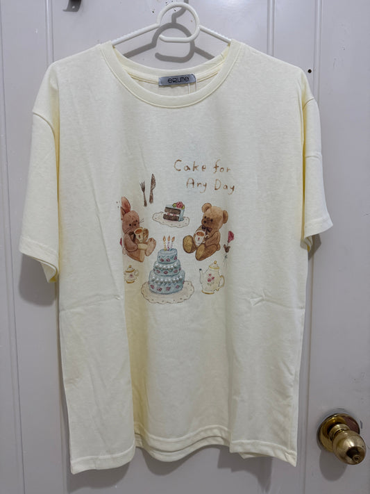 Close-up of teddy bear and rabbit enjoying tea beside a birthday cake printed on a cream cotton T-shirt