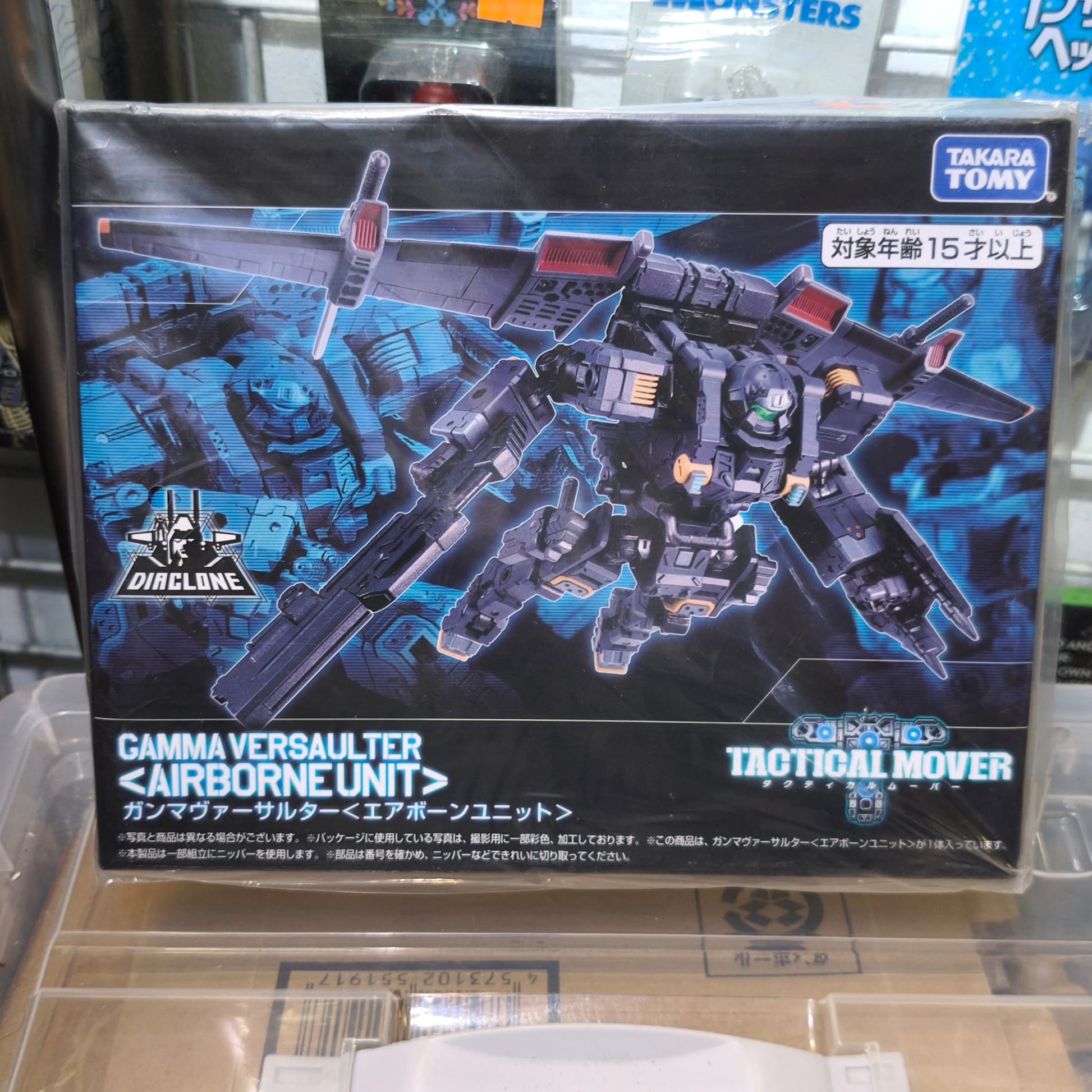 Front panel of the Takara Tomy Diaclone box featuring a dramatic illustration of the dark grey Gamma Versaulter Airborne Unit flying with its wings deployed against a high-tech blue grid background.