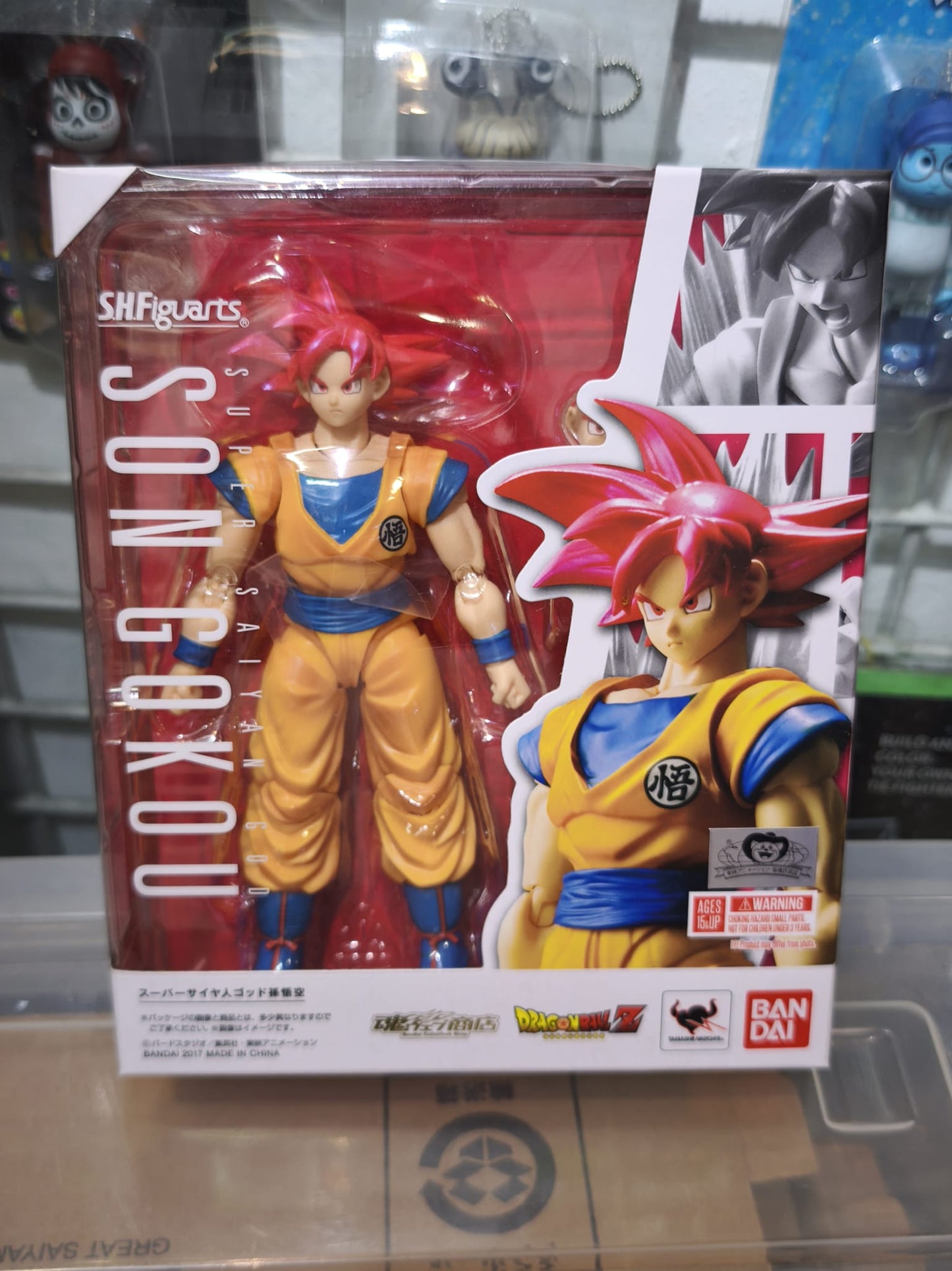 Front window box packaging of the Bandai S.H.Figuarts Super Saiyan God Son Goku action figure featuring a metallic Tamashii web shop quality emblem.