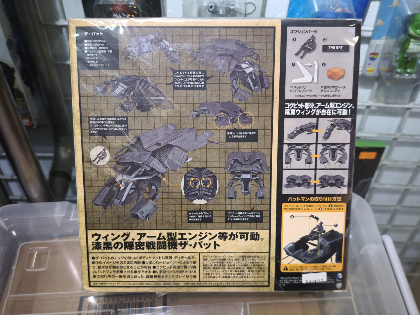 Front window box packaging of the Kaiyodo Sci-Fi Revoltech Series No. 051 The Bat vehicle from The Dark Knight Rises, displaying the matte black stealth aircraft, included mini Batman pilot figure, clear V-shaped display base, and movie logo branding.